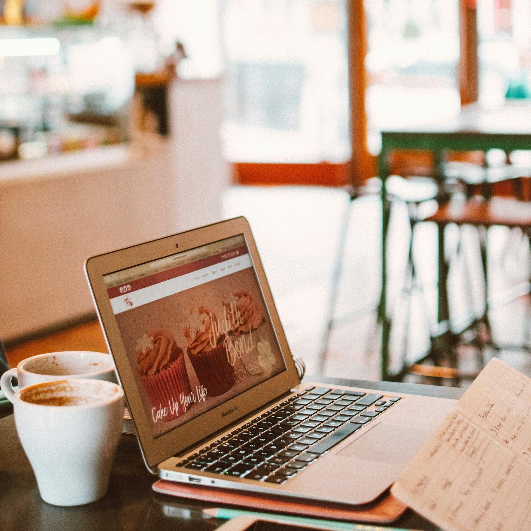 A cozy café setting with a laptop, coffee, and notebook, perfect for working or blogging.